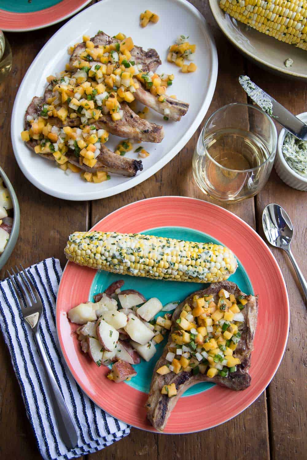 brightly colored dinner plate with pork chops, corn on the cob, and potato salad.