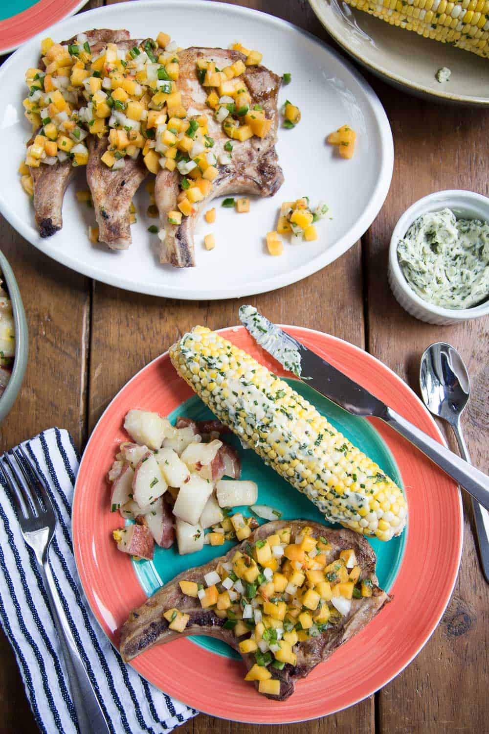 green and pink plate filled with pork chops with nectarine salsa, corn on the cob, and potato salad.