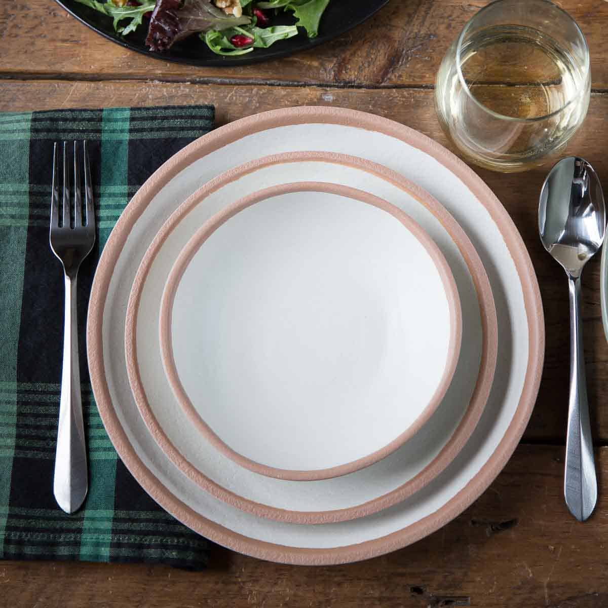 matching plates and bowl on a wooden table with a plaid napkin and silverware.
