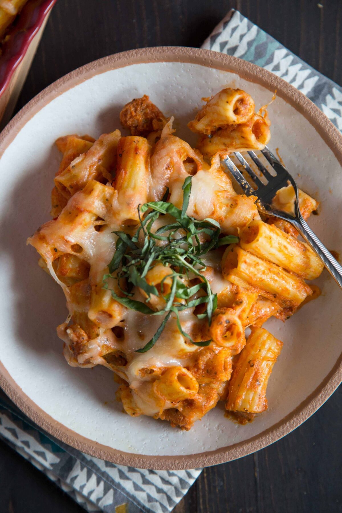 baked ziti in a cream and brown bowl, topped with basil.