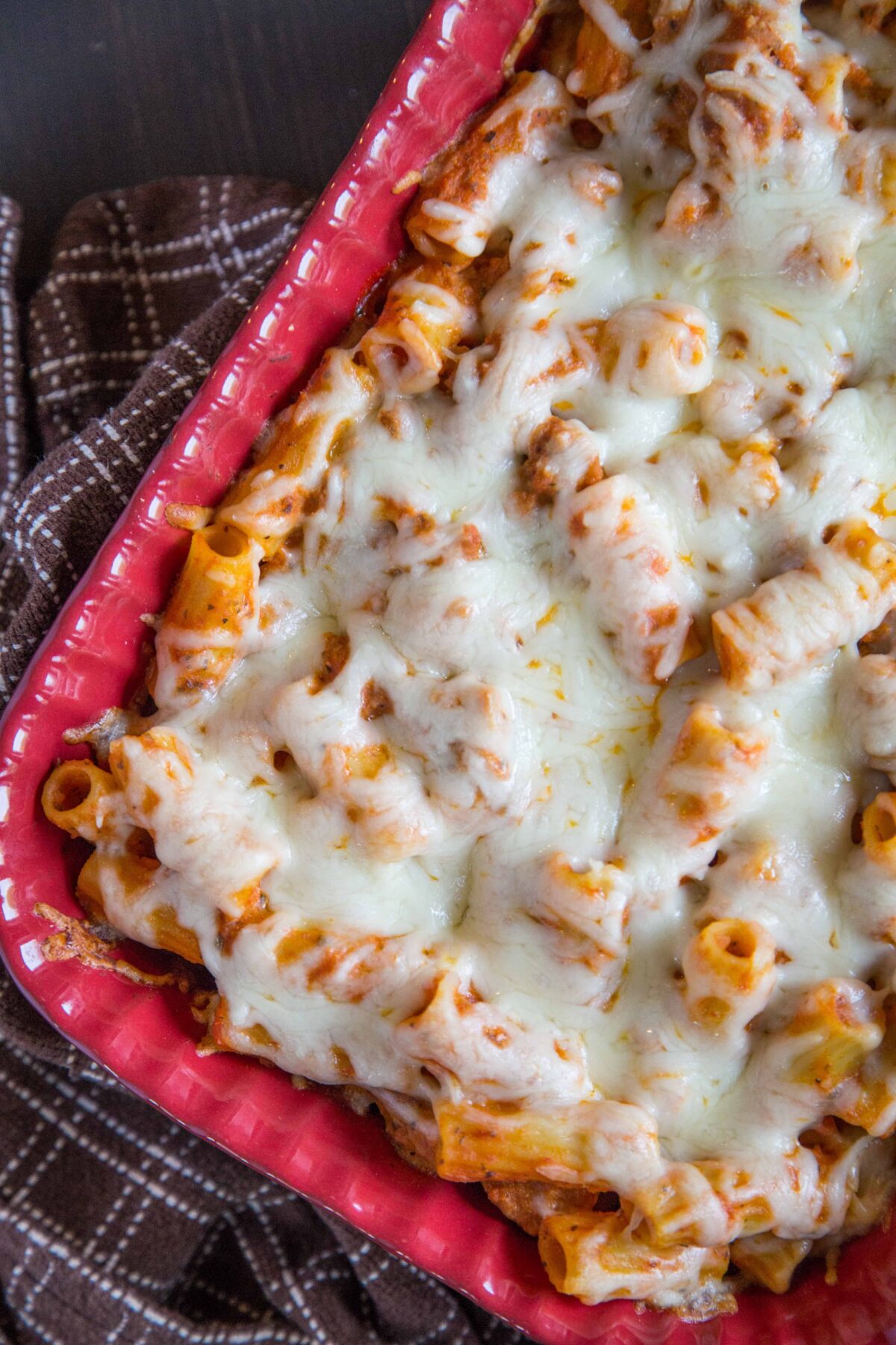 red casserole dish filled with baked ziti and topped with cheese.