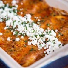 enchiladas with red sauce and crumbled queso fresco in a blue casserole dish.