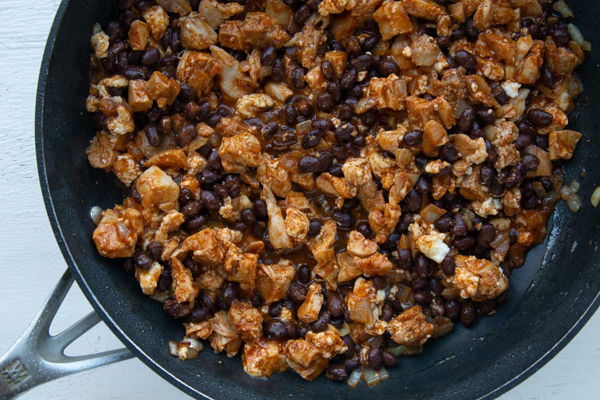 chopped chicken and black beans in a red enchilada sauce in a skillet.