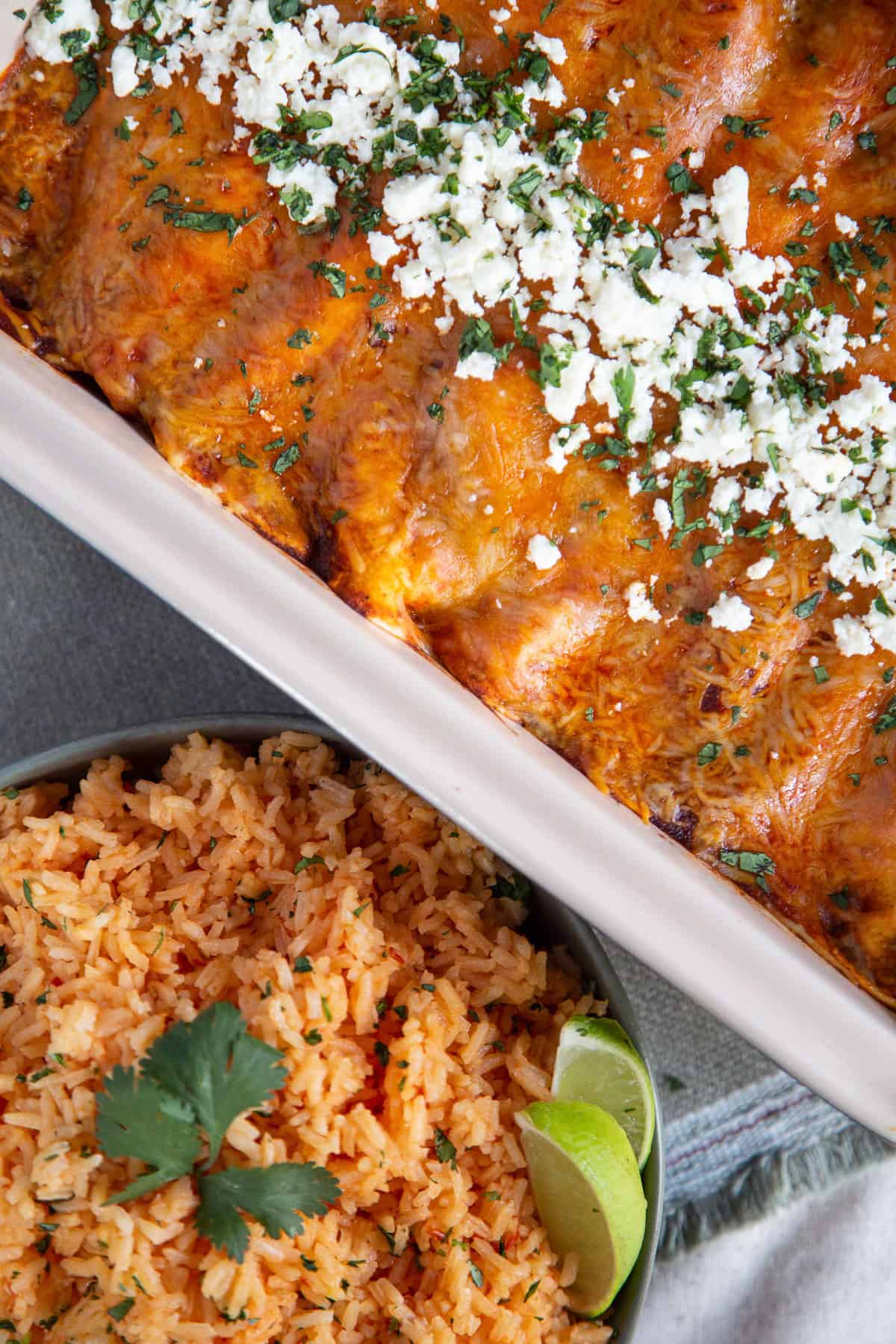 a pan of enchiladas next to a bowl of mexican rice.