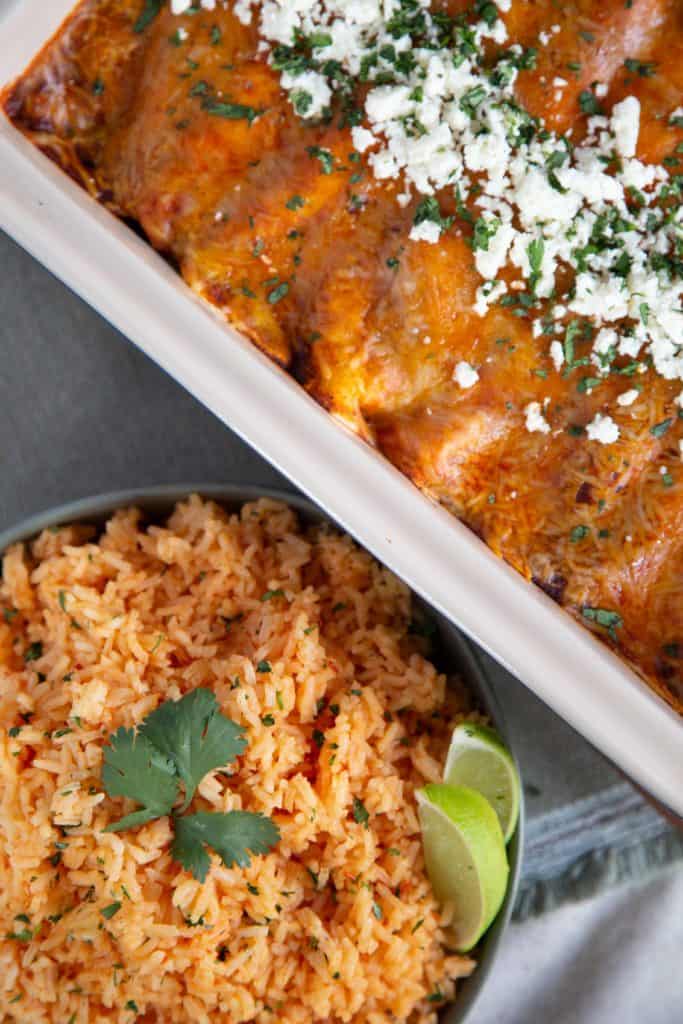 bowl of mexican rice and a casserole dish with enchiladas on a cream tablecloth