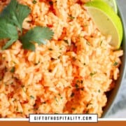orange hued mexican rice in a green dish, topped with a sprig of cilantro.