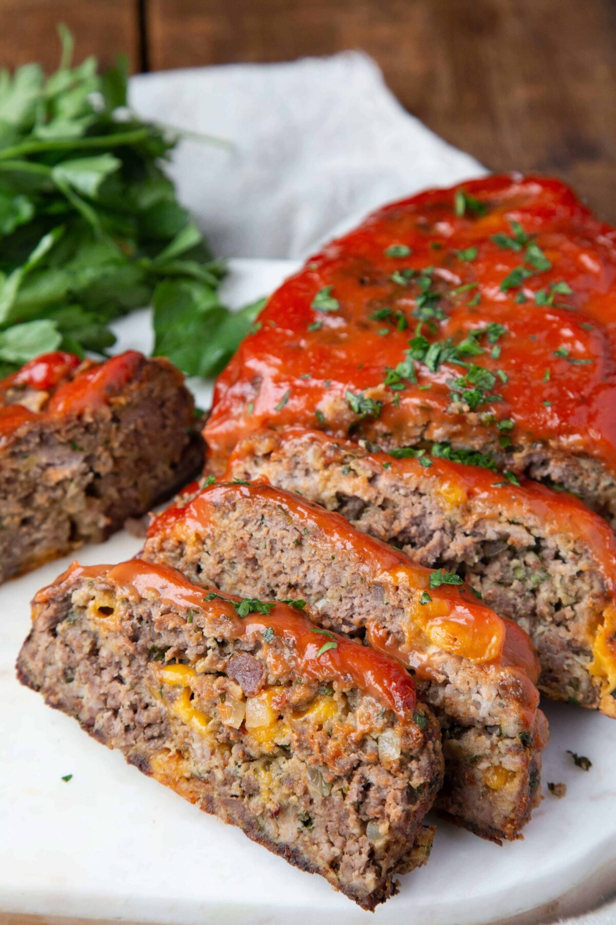 slices of bacon cheddar meatloaf on a white platter topped with ketchup and parsley.