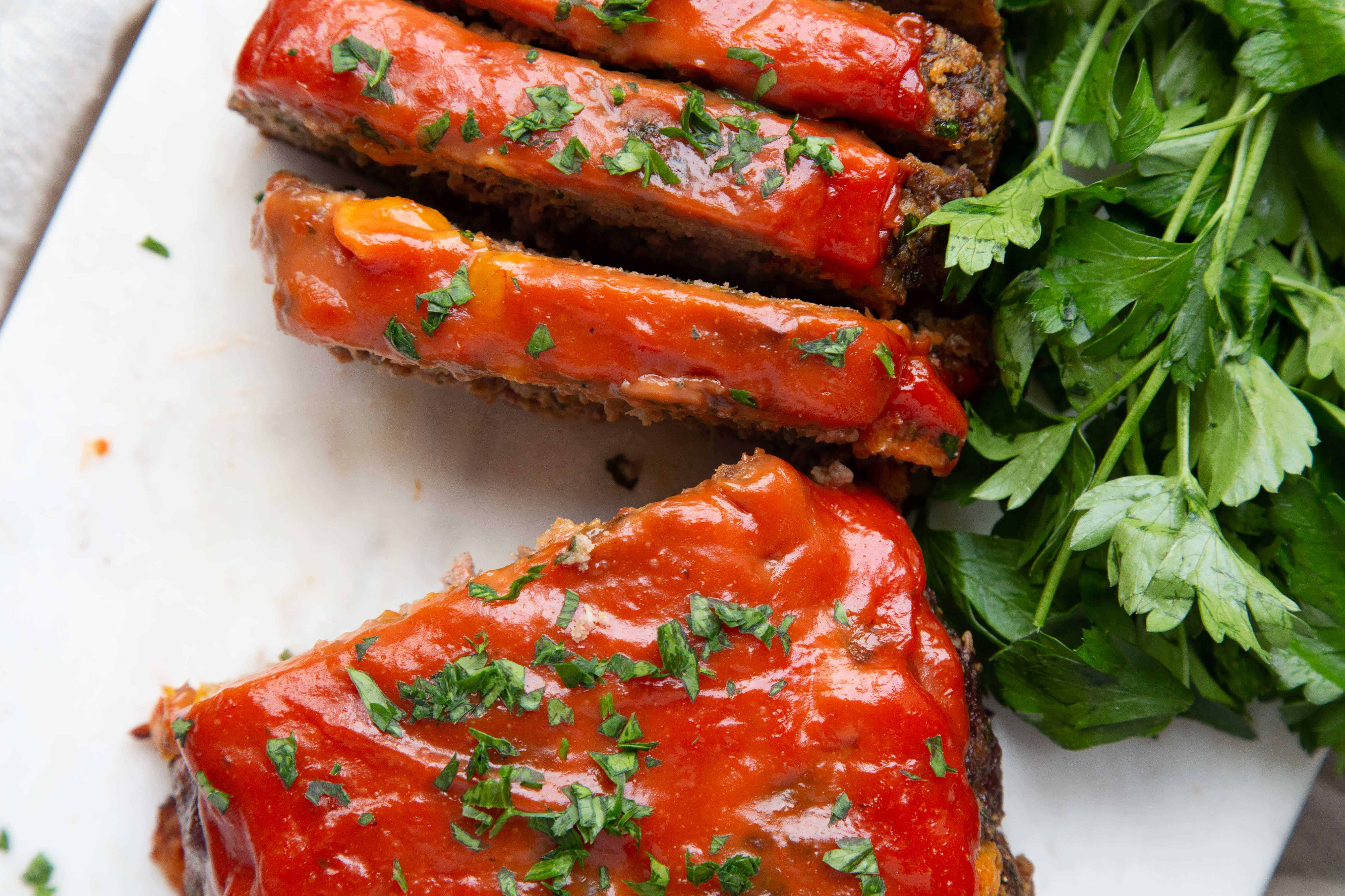 slices of bacon cheddar meatloaf on a white marble board with fresh parsley.