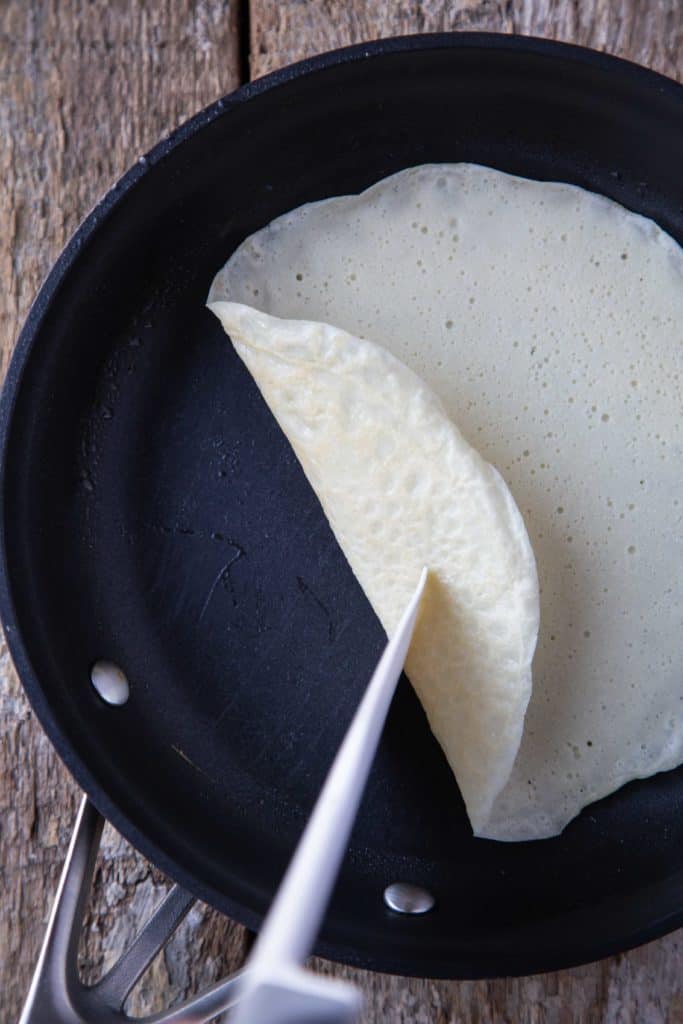 spatula lifting a corner of a crepe out of a nonstick skillet.