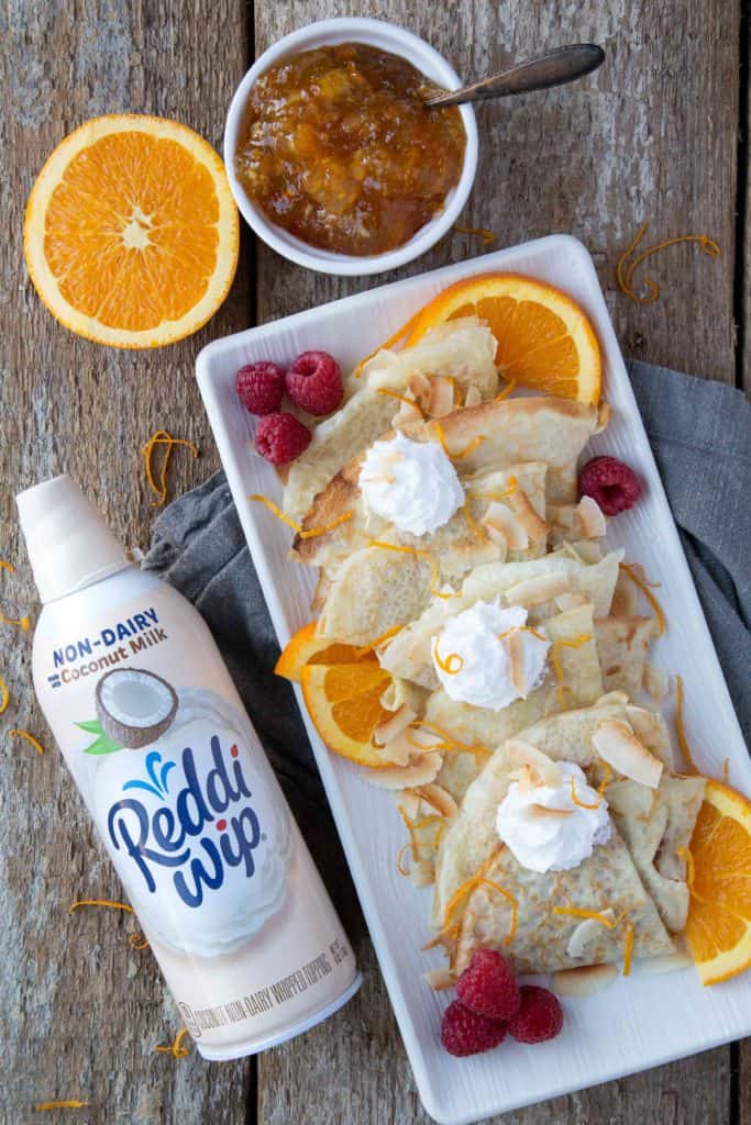 Coconut Milk Crepes on a platter with whipped cream and raspberries, with a can of non-dairy whipped cream on the side.