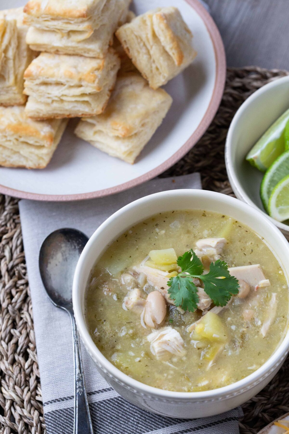 a bowl of white chicken chili with flaky biscuits in the background