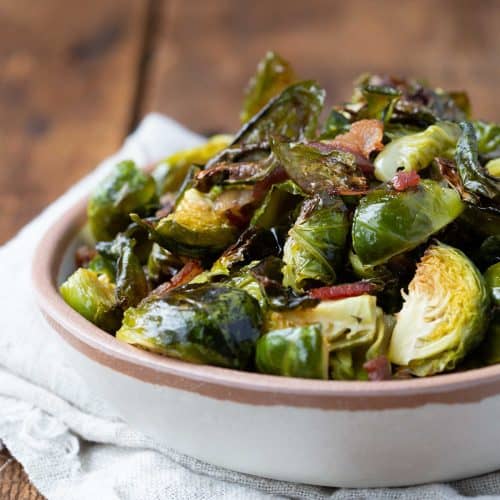 bacon brussels sprouts in a cream bowl on a wooden table.