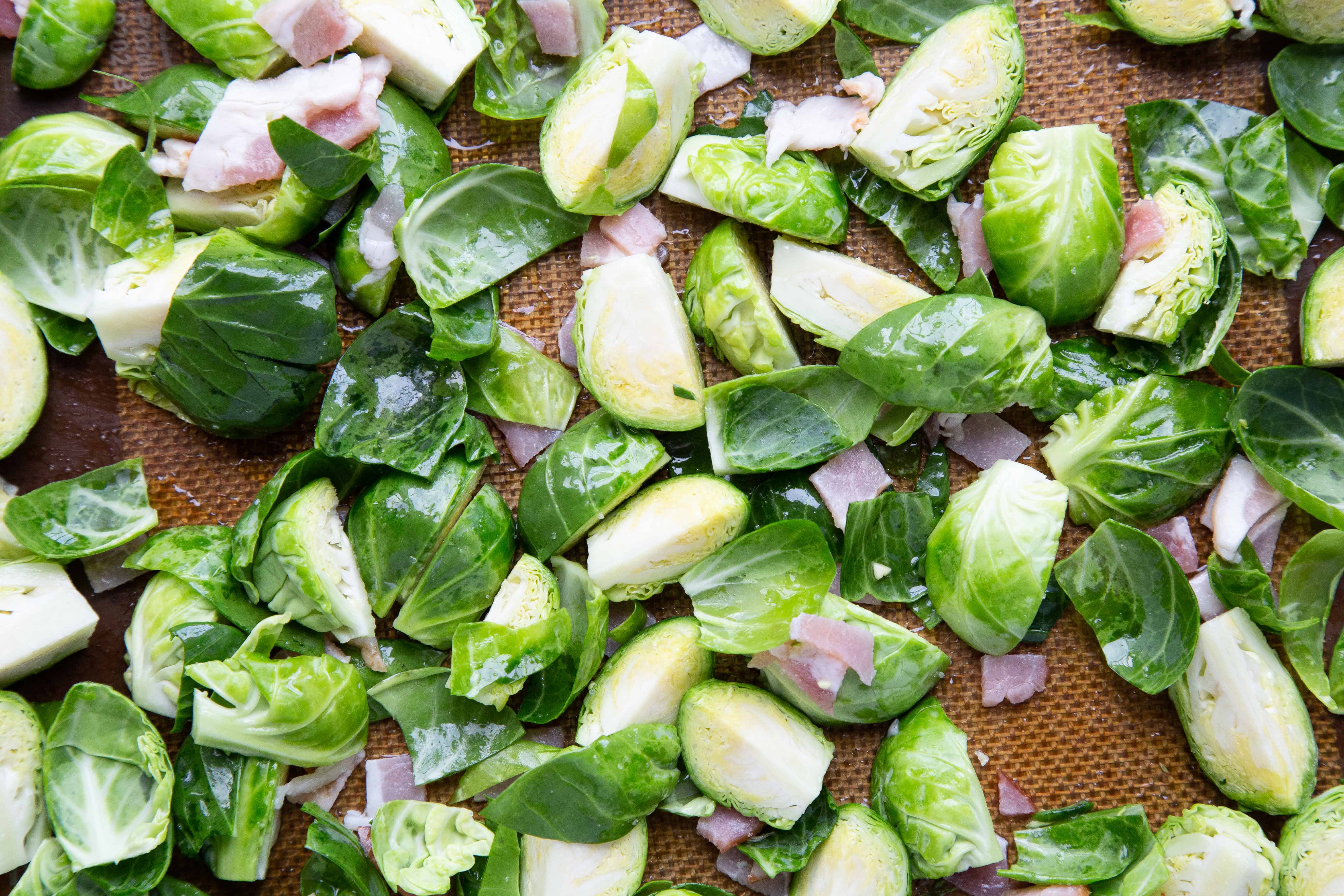 raw brussels sprouts tossed with bacon on a sheet pan.