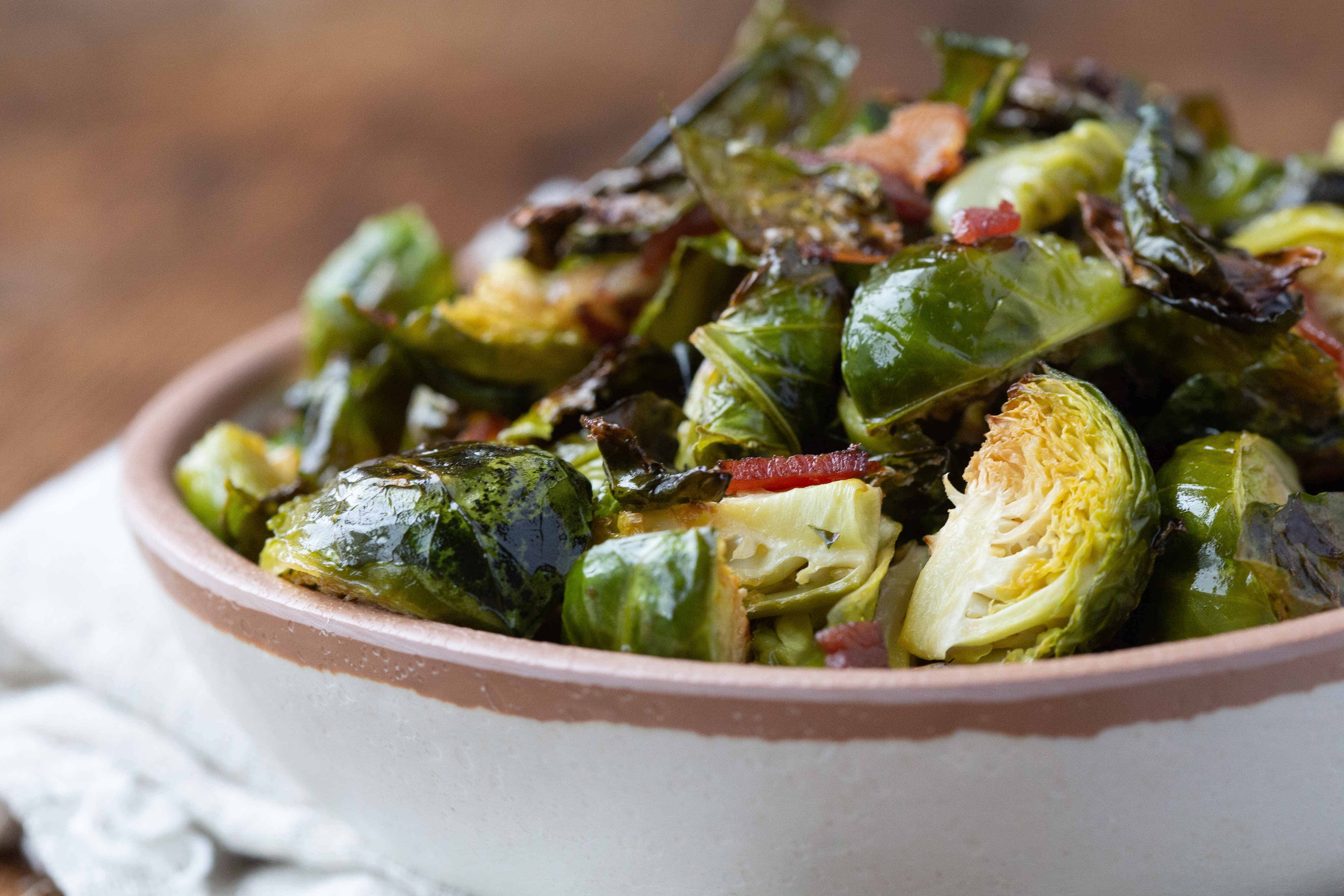 Bacon Brussels Sprouts in a cream and brown bowl on a wooden table.