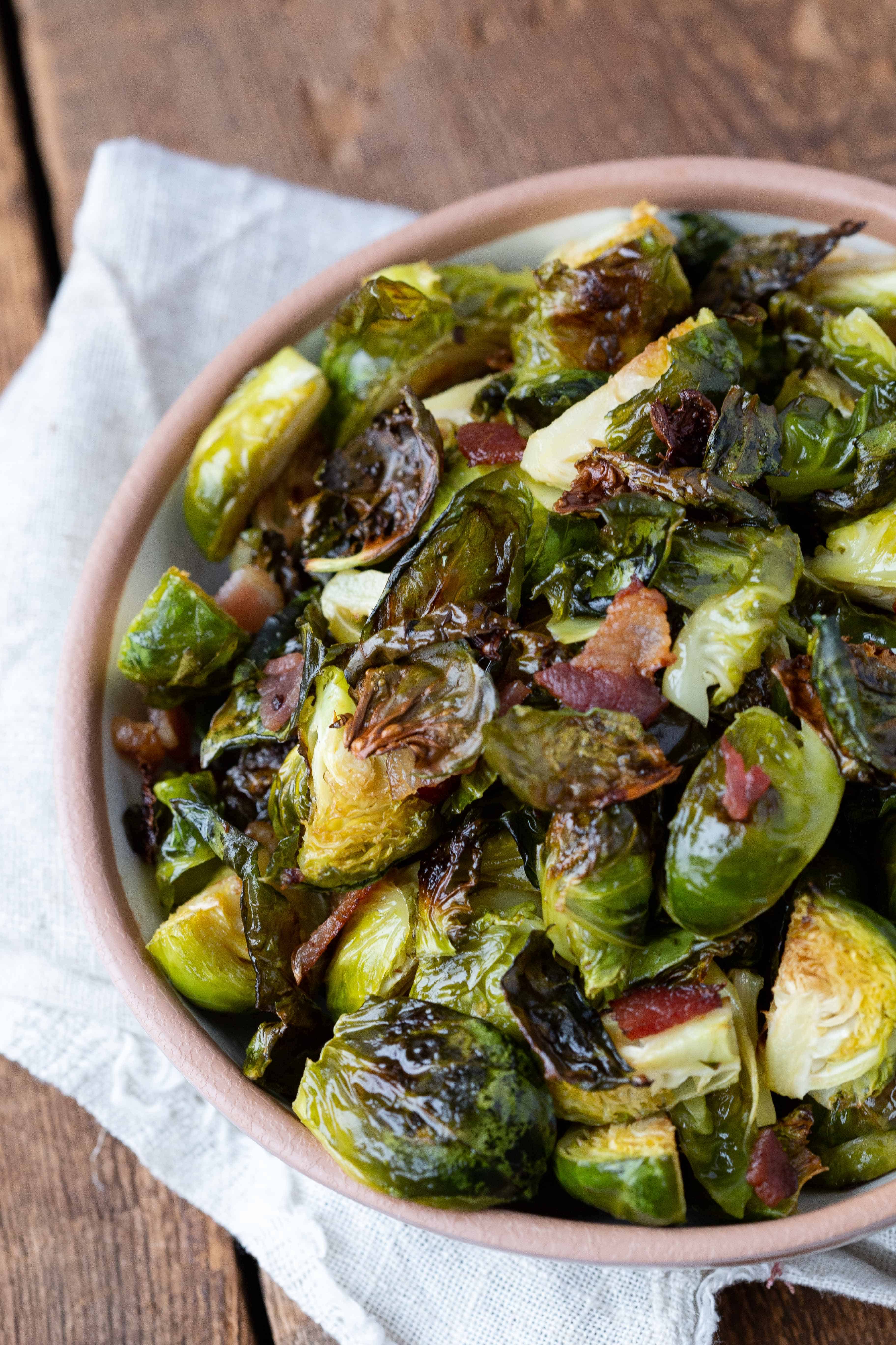 Bacon Brussels Sprouts in a brown bowl with a white tea towel underneath.