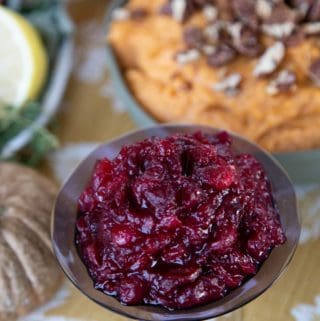 Apple Cranberry Sauce in a glass dish on a colorful Thanksgiving table.