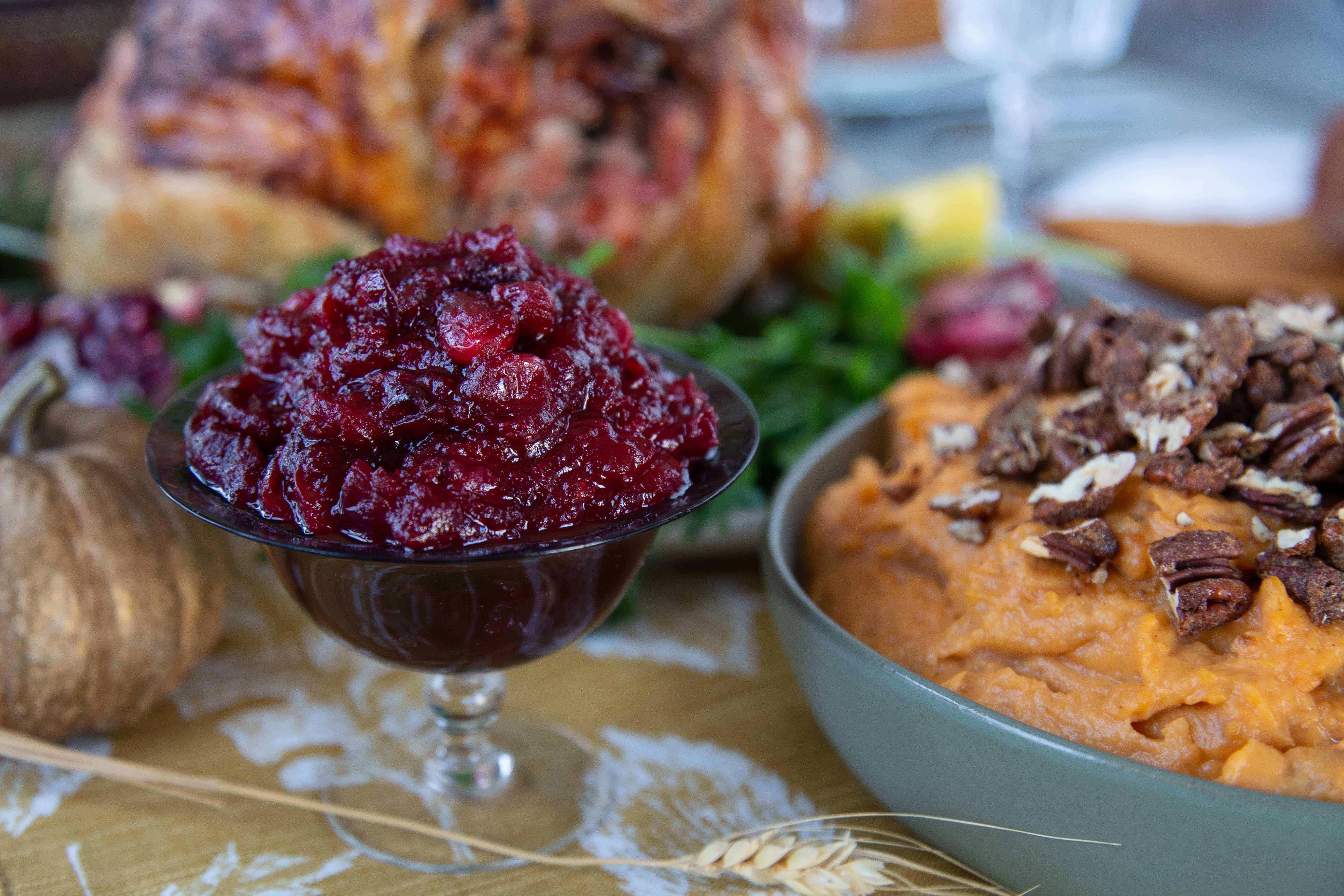 Apple Cranberry Sauce in a footed glass dish next to a bowl of mashed sweet potatoes.