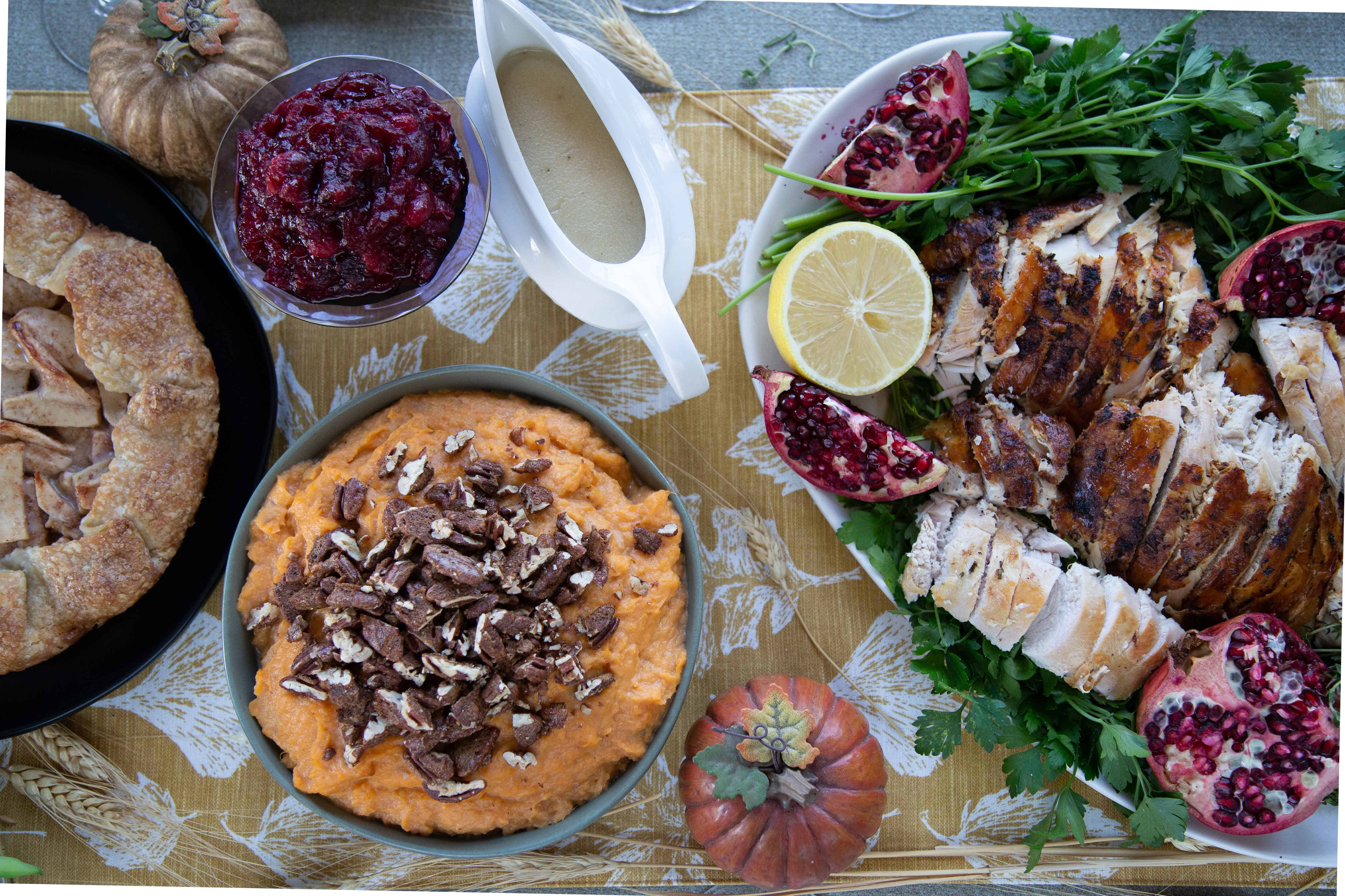 Thanksgiving table with turkey, sweet potatoes, cranberry sauce, and gravy.