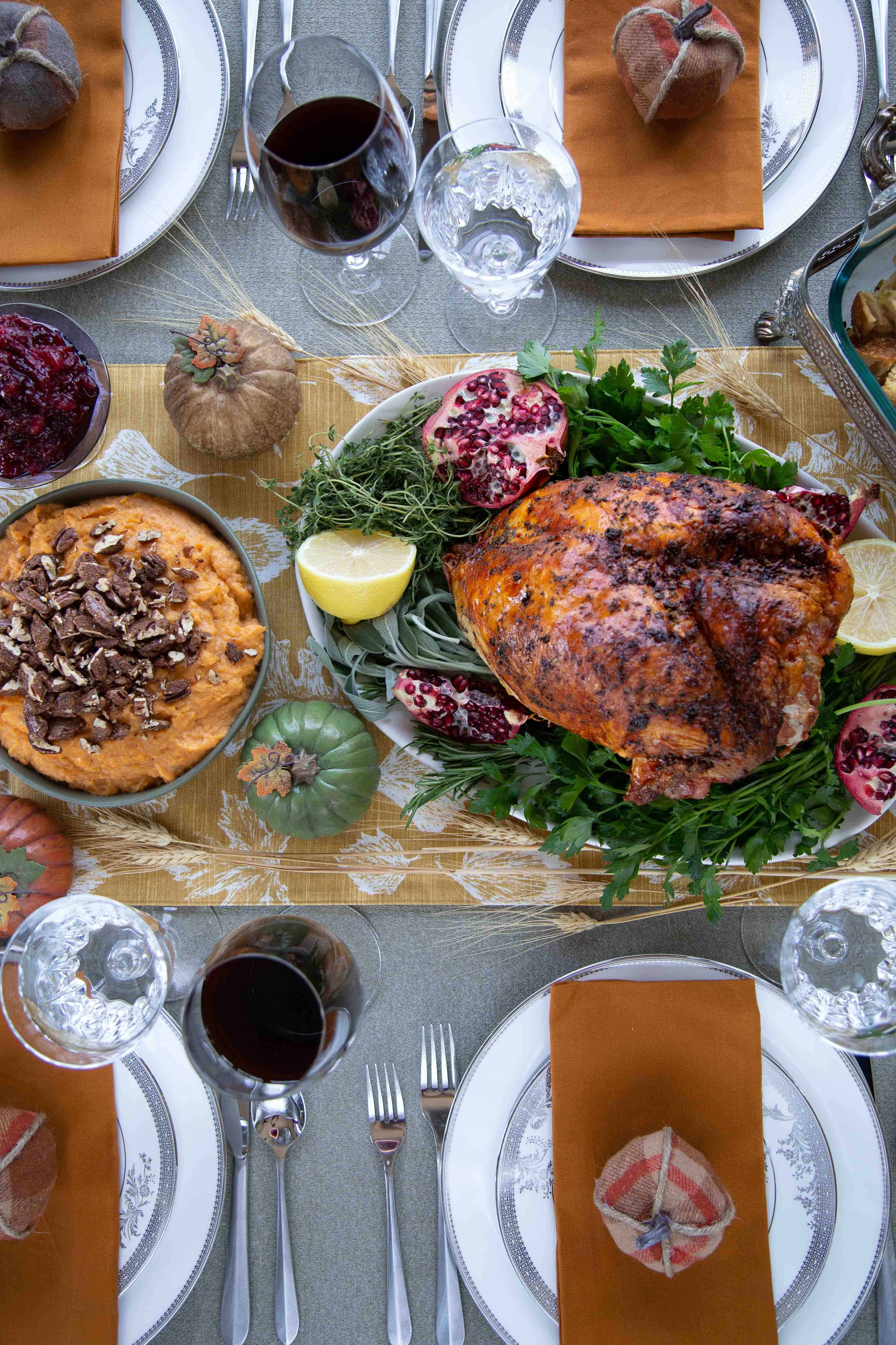 Thanksgiving tablescape with a bone-in turkey breast, mashed sweet potatoes, mini faux pumpkins, and china. 