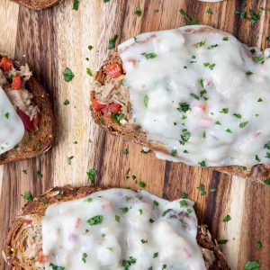 italian tuna melts with melted cheese and chopped parsley on a wooden board.