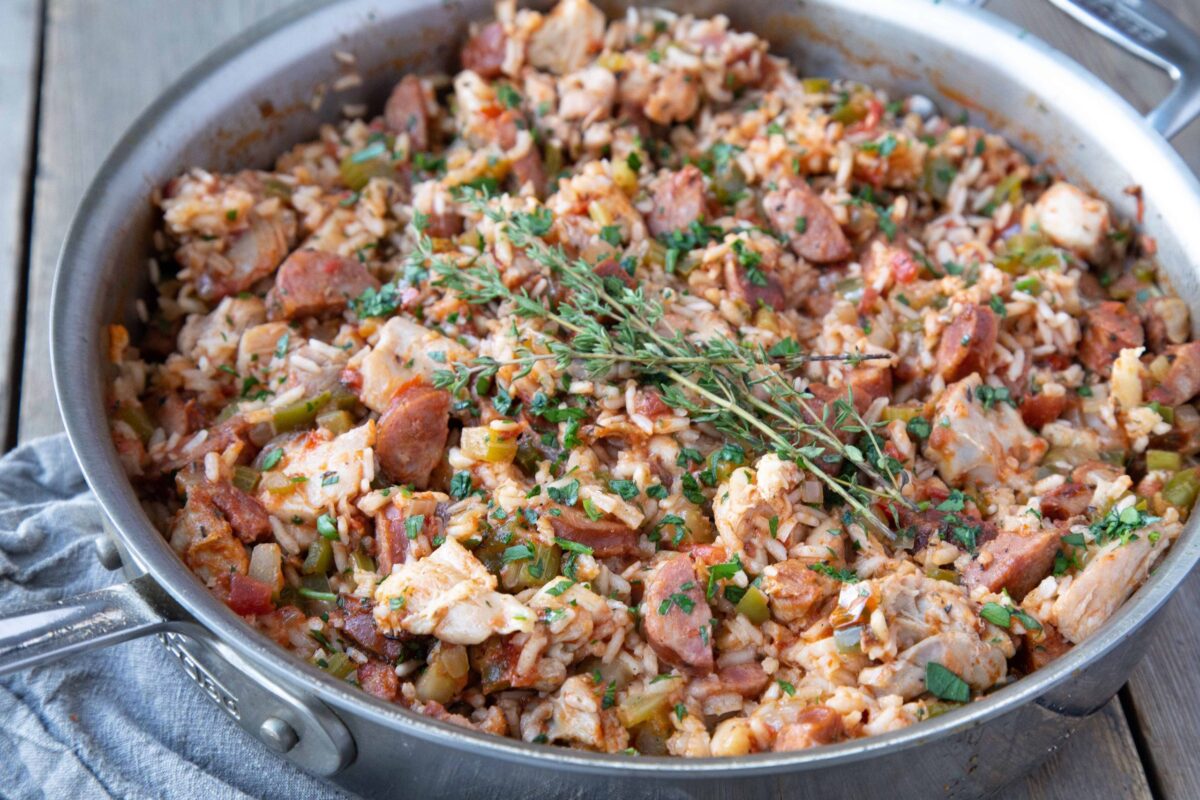 metal pan of chicken and sausage jambalaya topped with fresh thyme.