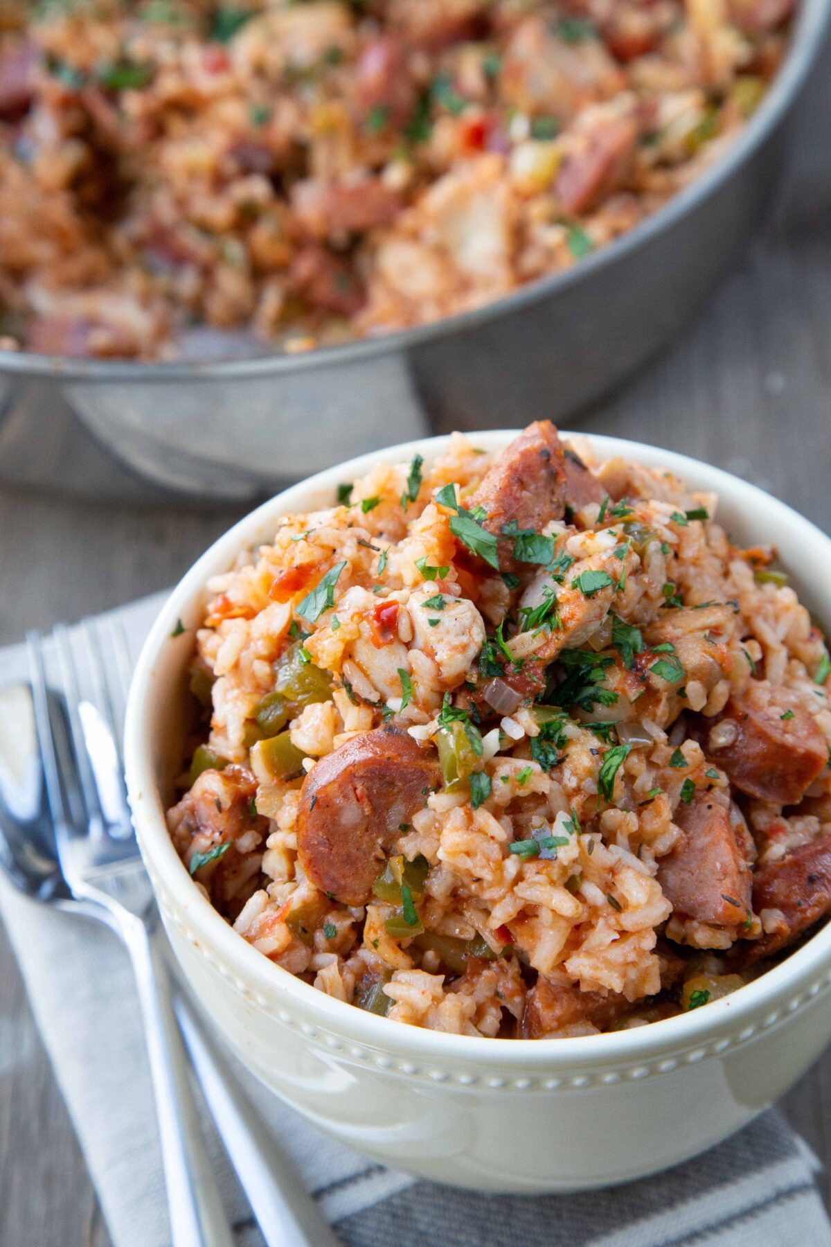 yellow bowl of chicken and sausage jambalaya in front of a pan with more jambalaya.