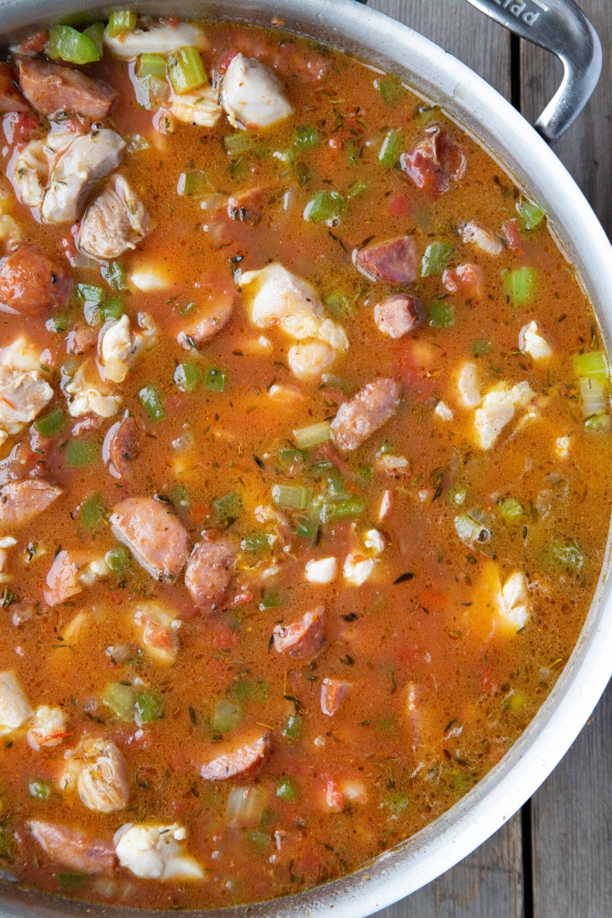 chicken, sausage, chopped bell peppers, and celery in a tomato broth in a sauté pan.