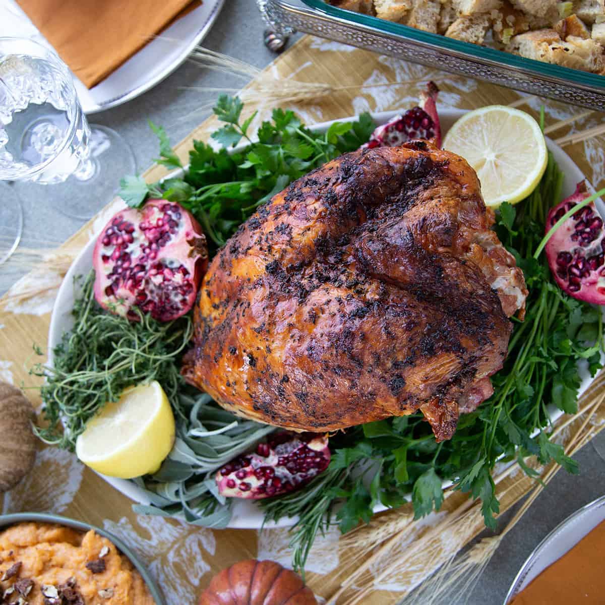 cooked turkey breast on a platter with herbs, lemons, and pomegranate halves.