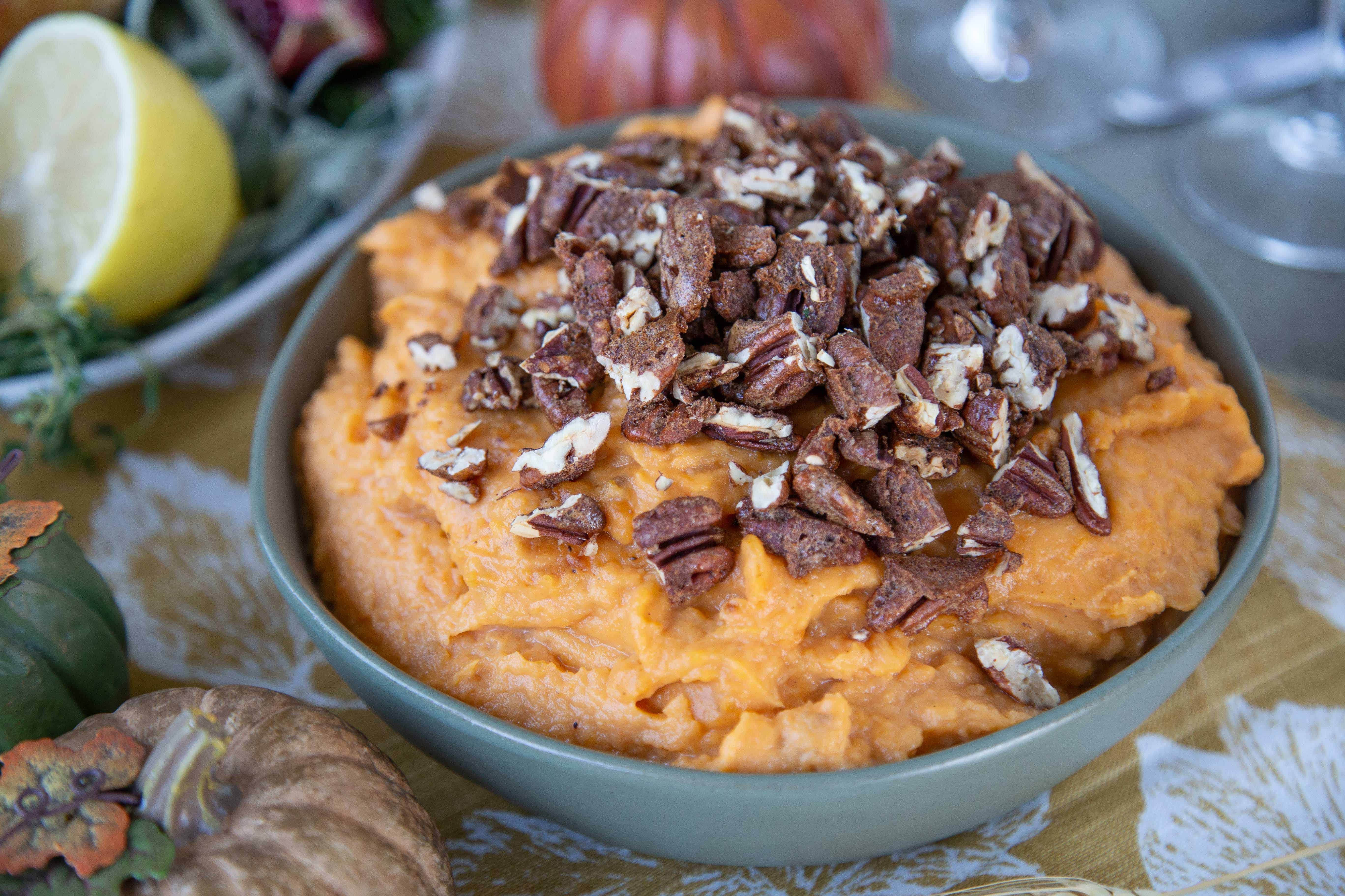 Mashed Sweet Potatoes with Spiced Pecans in a green bowl on a table with gold, green, and orange faux pumpkins.