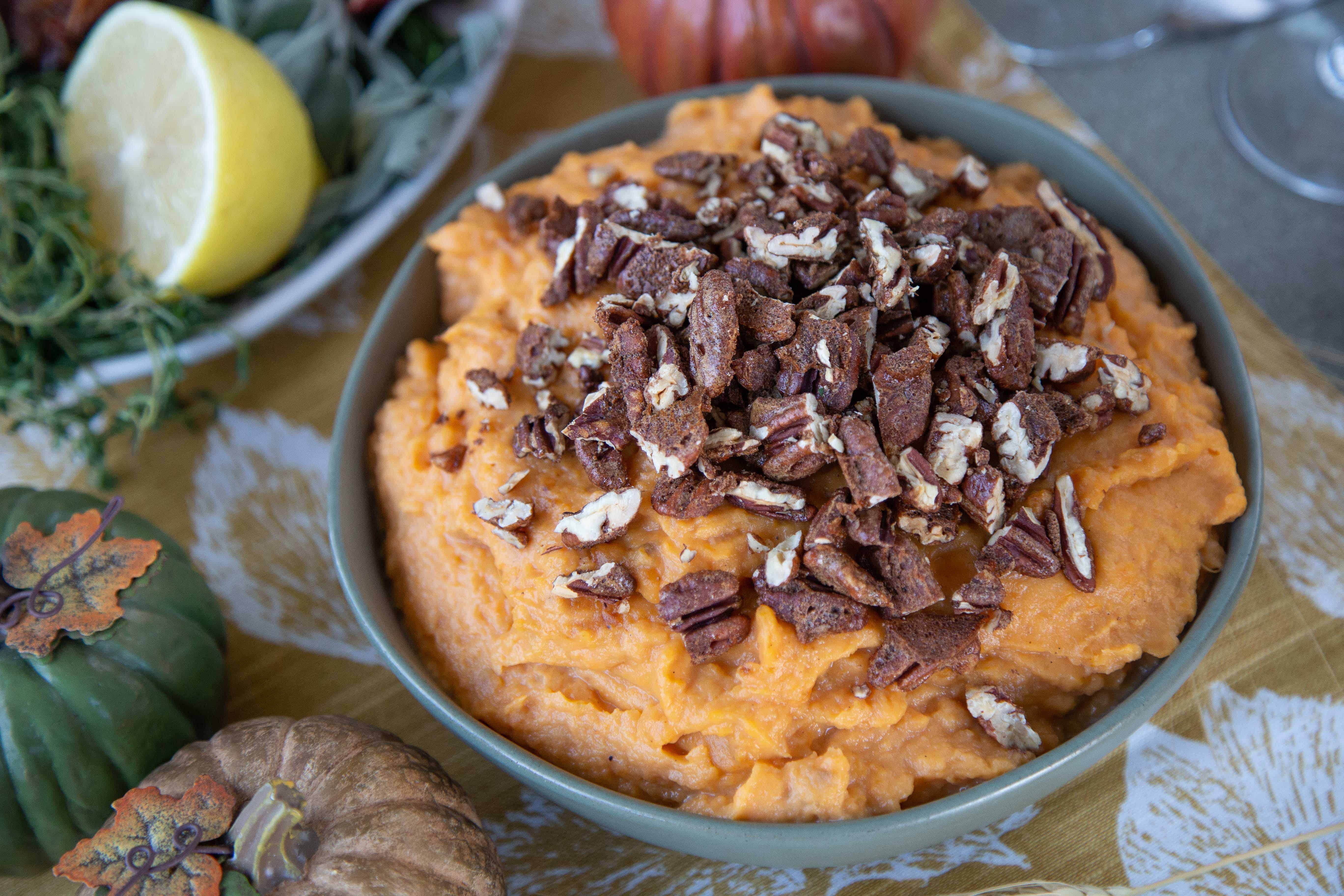 sweet potatoes topped with candied pecans in a green bowl on a thanksgiving table.