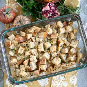 vegan stuffing in a casserole dish, sitting on a yellow and white table runner with mini pumpkins nearby.