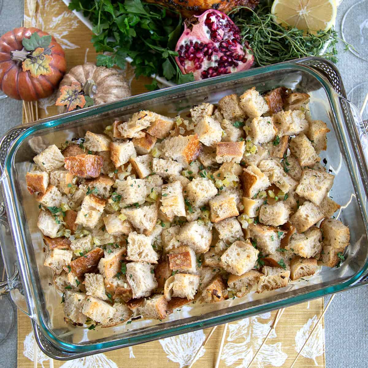 vegan stuffing in a casserole dish, sitting on a yellow and white table runner with mini pumpkins nearby.