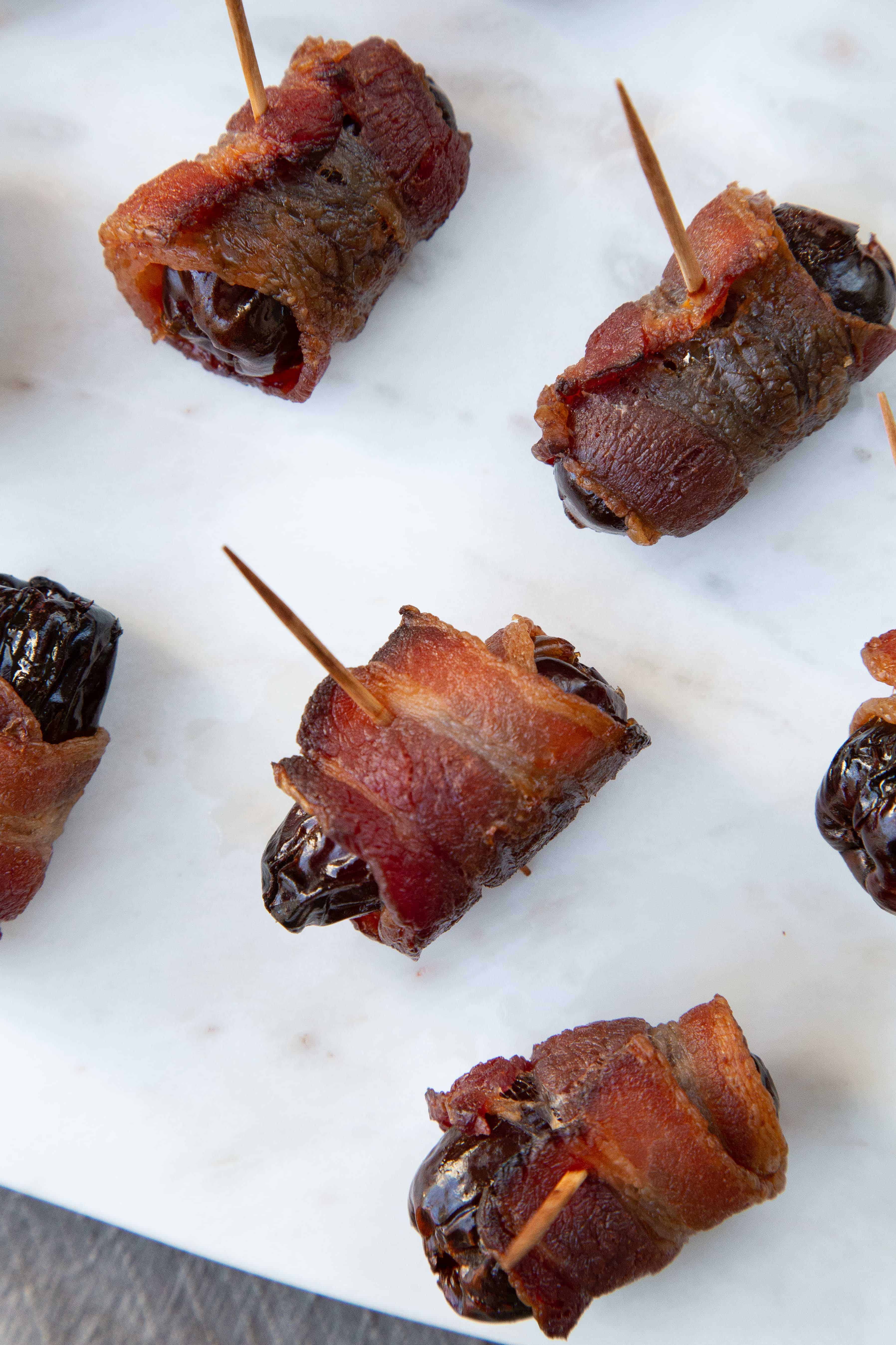 Bacon Wrapped Dates on a white marble tray.