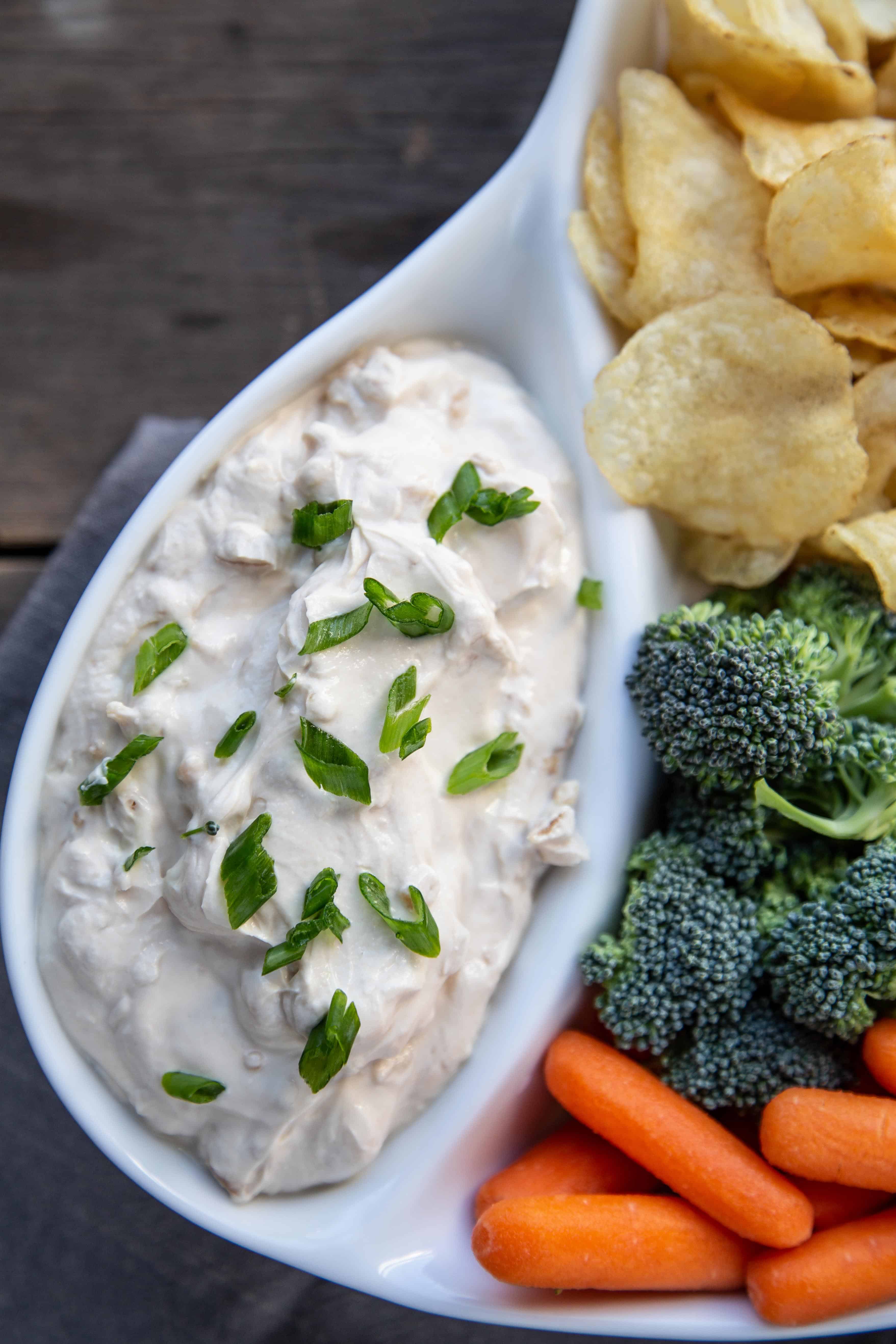 French onion dip in a white dish with raw veggies and potato chips.
