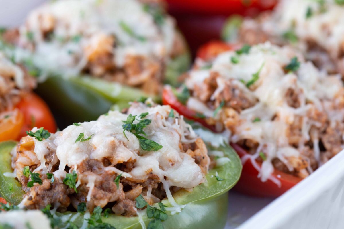 close up of Italian Stuffed Peppers topped with cheese and chopped parsley in a white casserole dish.