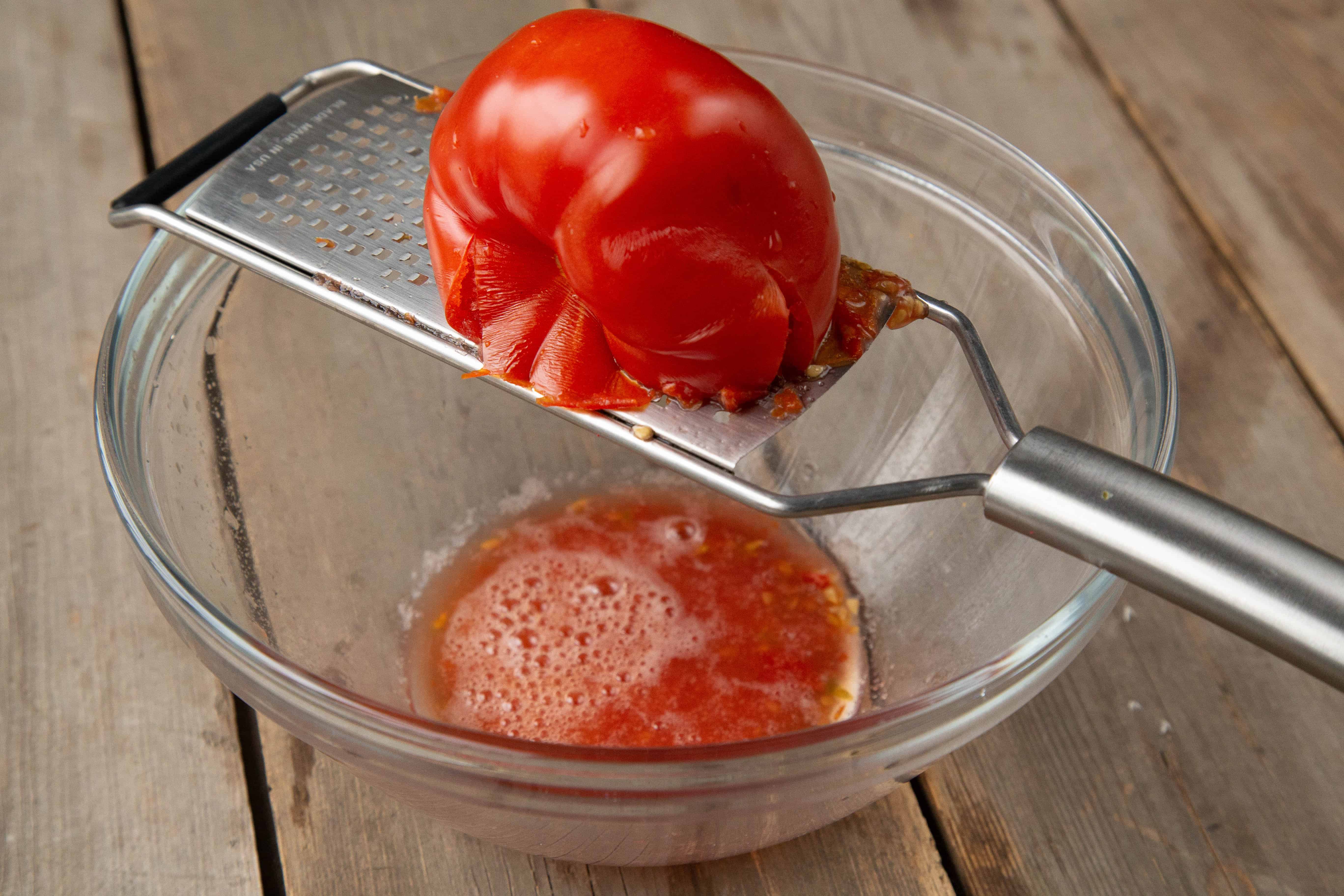 Grating a Tomato on a handheld grater over a glass bowl.