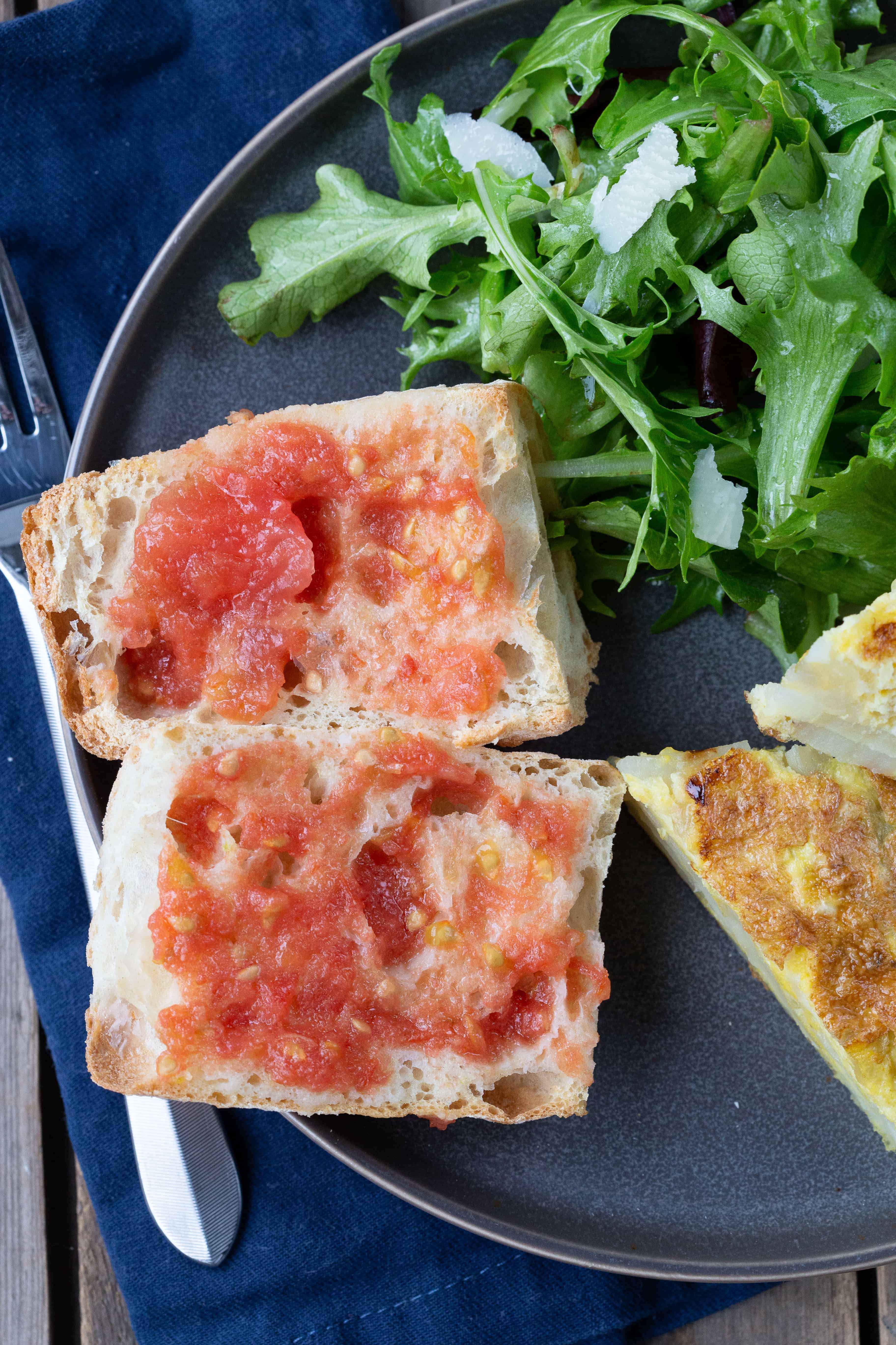Pan con Tomate on a gray plate with tortilla espanola and a green salad.