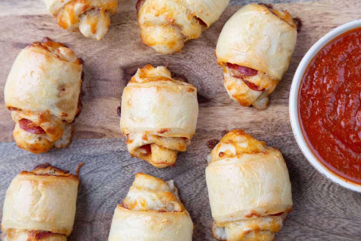 pepperoni rolls on a wooden board with a small dish of marinara