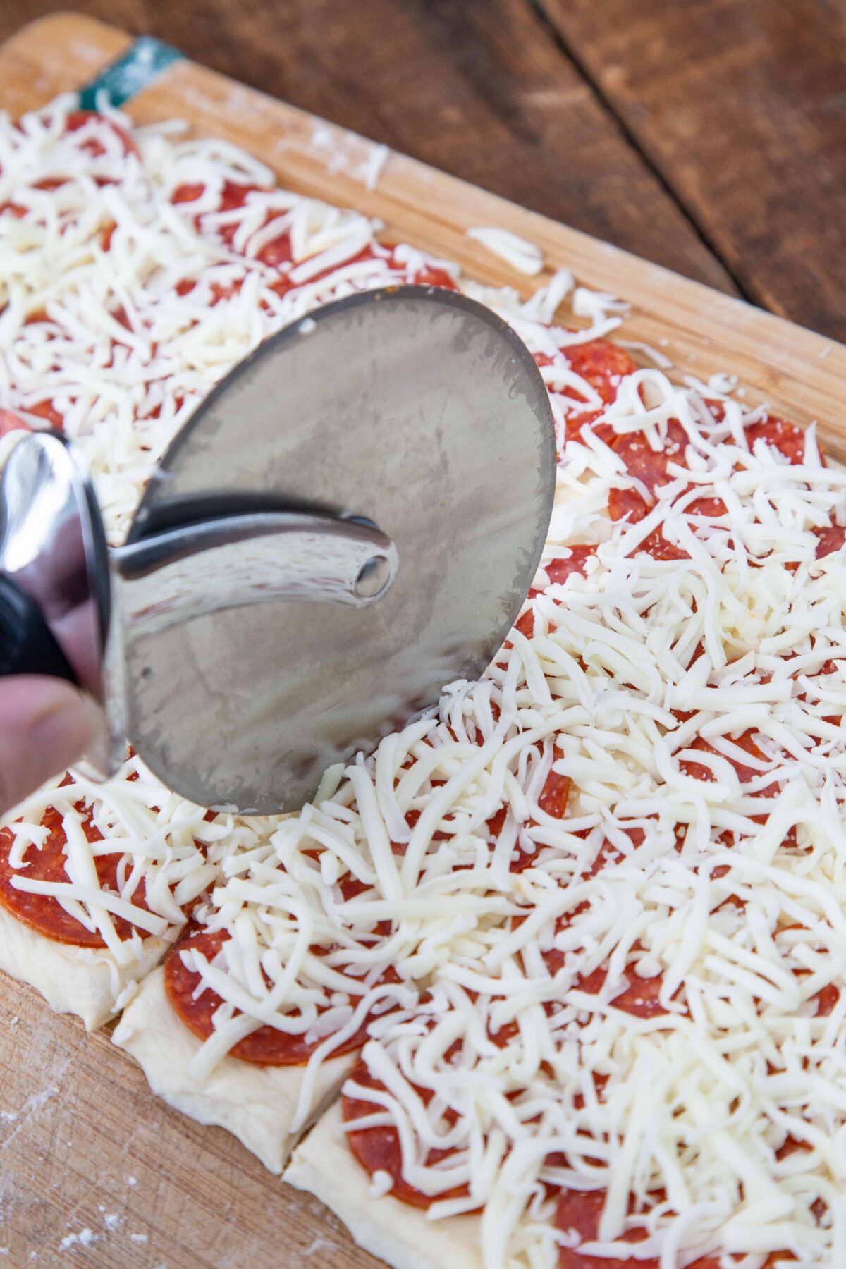 pizza wheel cutting through pizza dough topped with pepperoni and cheese.