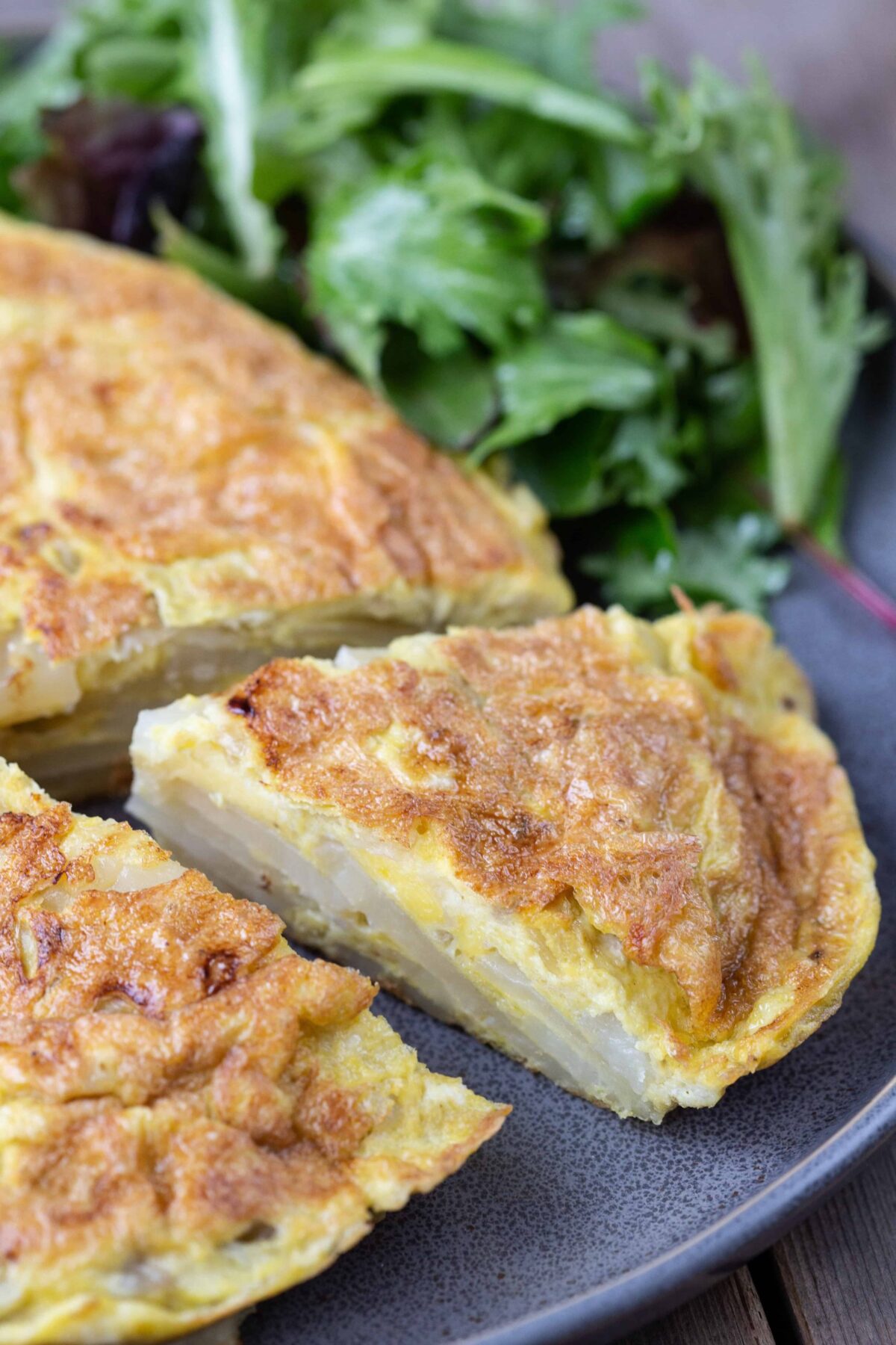 slice of Tortilla Espanola (Spanish Potato Omelette) taken out of a whole omelette on a gray plate.