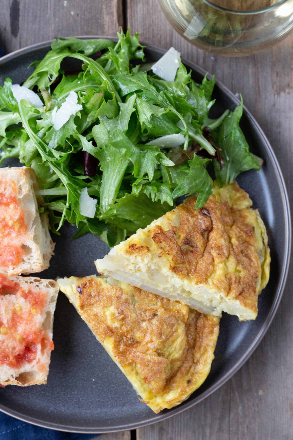 two slices of potato omelette on a plate with a salad and tomato bread.