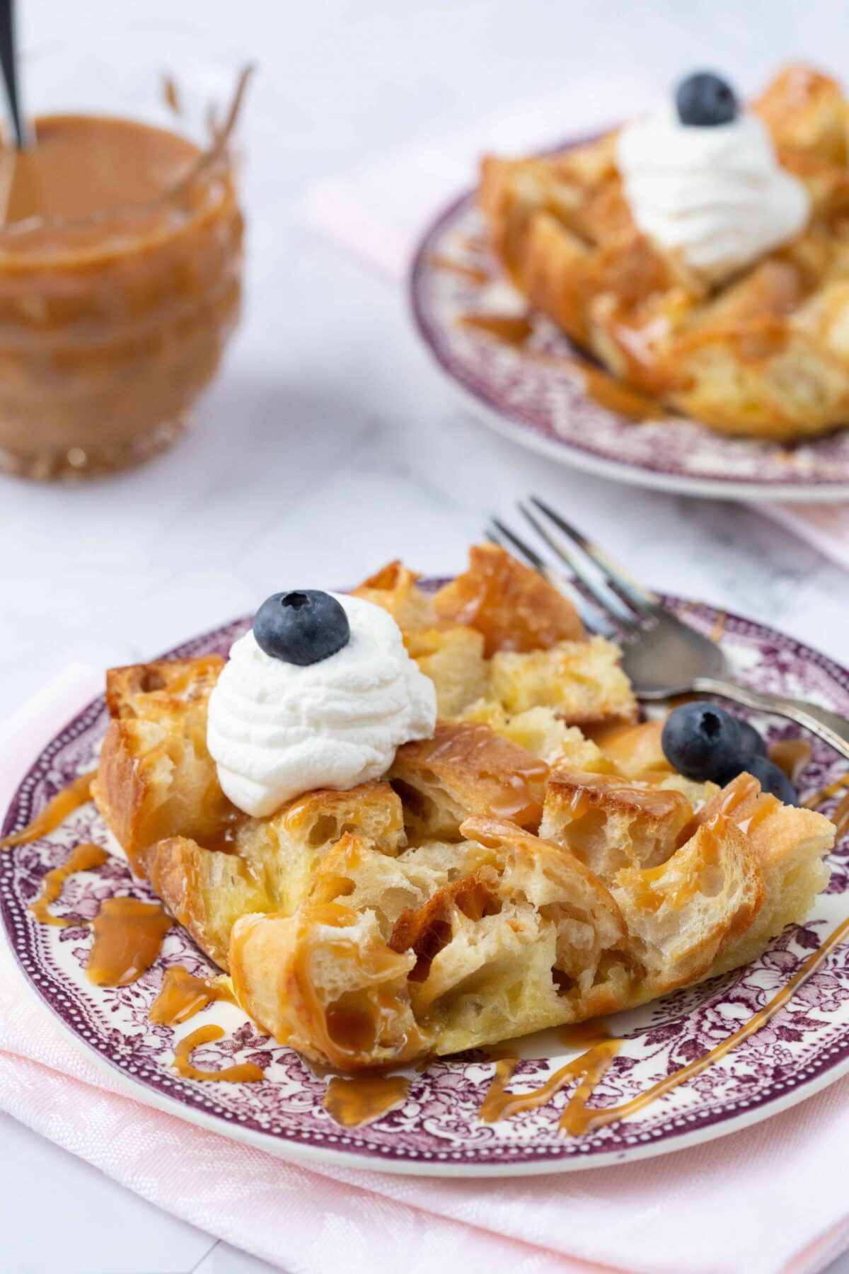 Bread Pudding for two on a purple patterned plate, topped with whipped cream and blueberries.