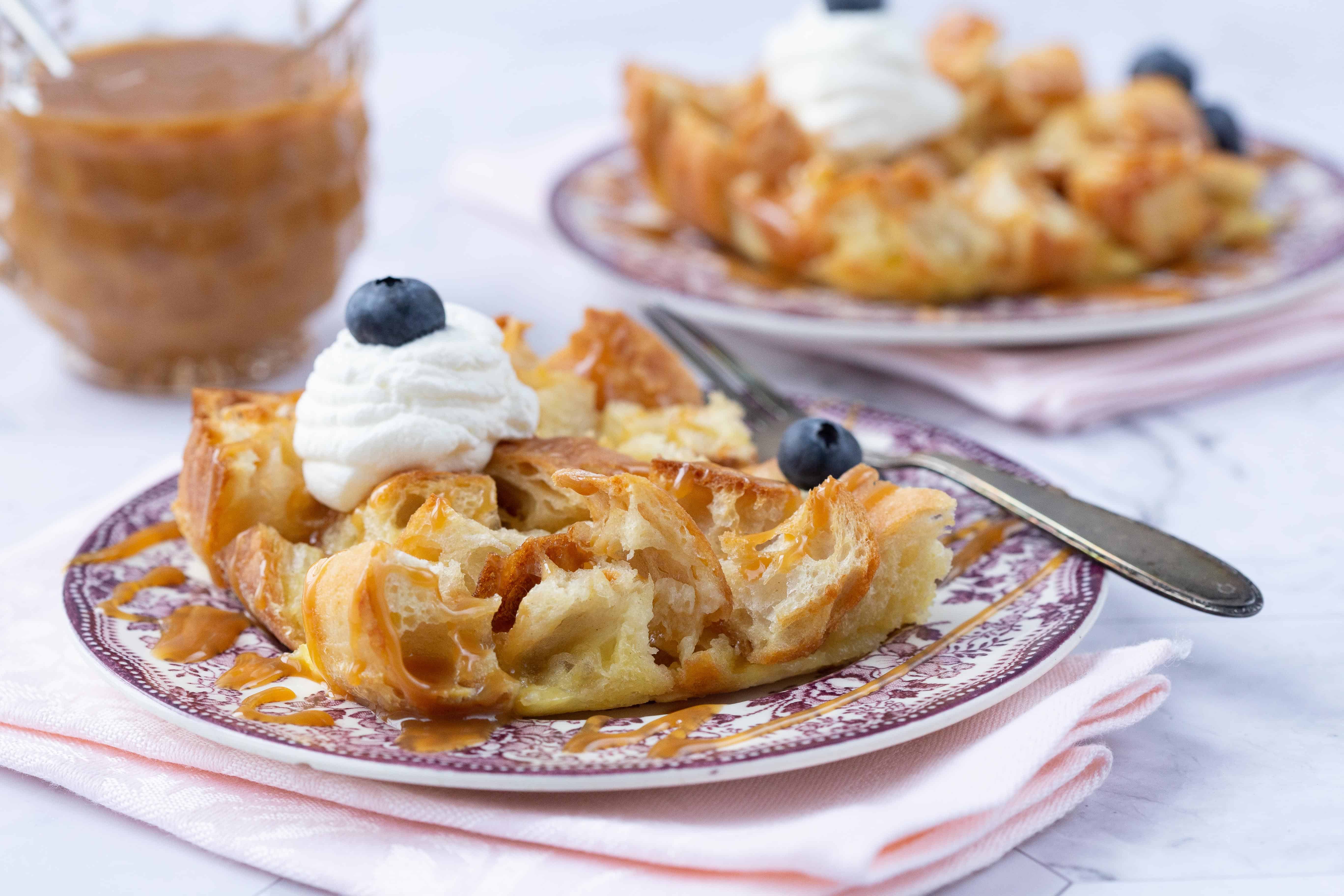 Bread Pudding slice on a purple plate with whipped cream and blueberries.