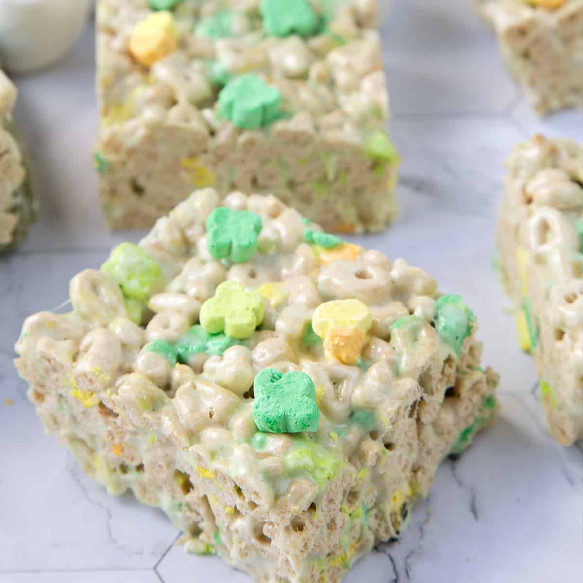 squares of marshmallow treats made with lucky charms on a white marble table.