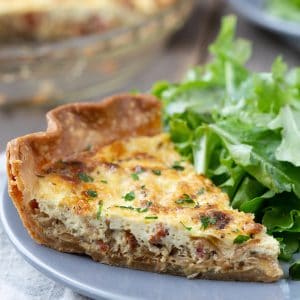 slice of alsatian quiche on a gray plate with a leafy green salad.