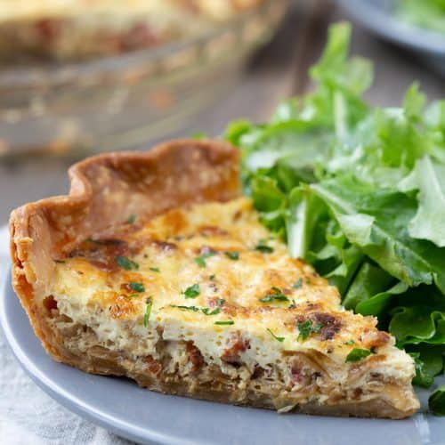 slice of alsatian quiche on a gray plate with a leafy green salad.