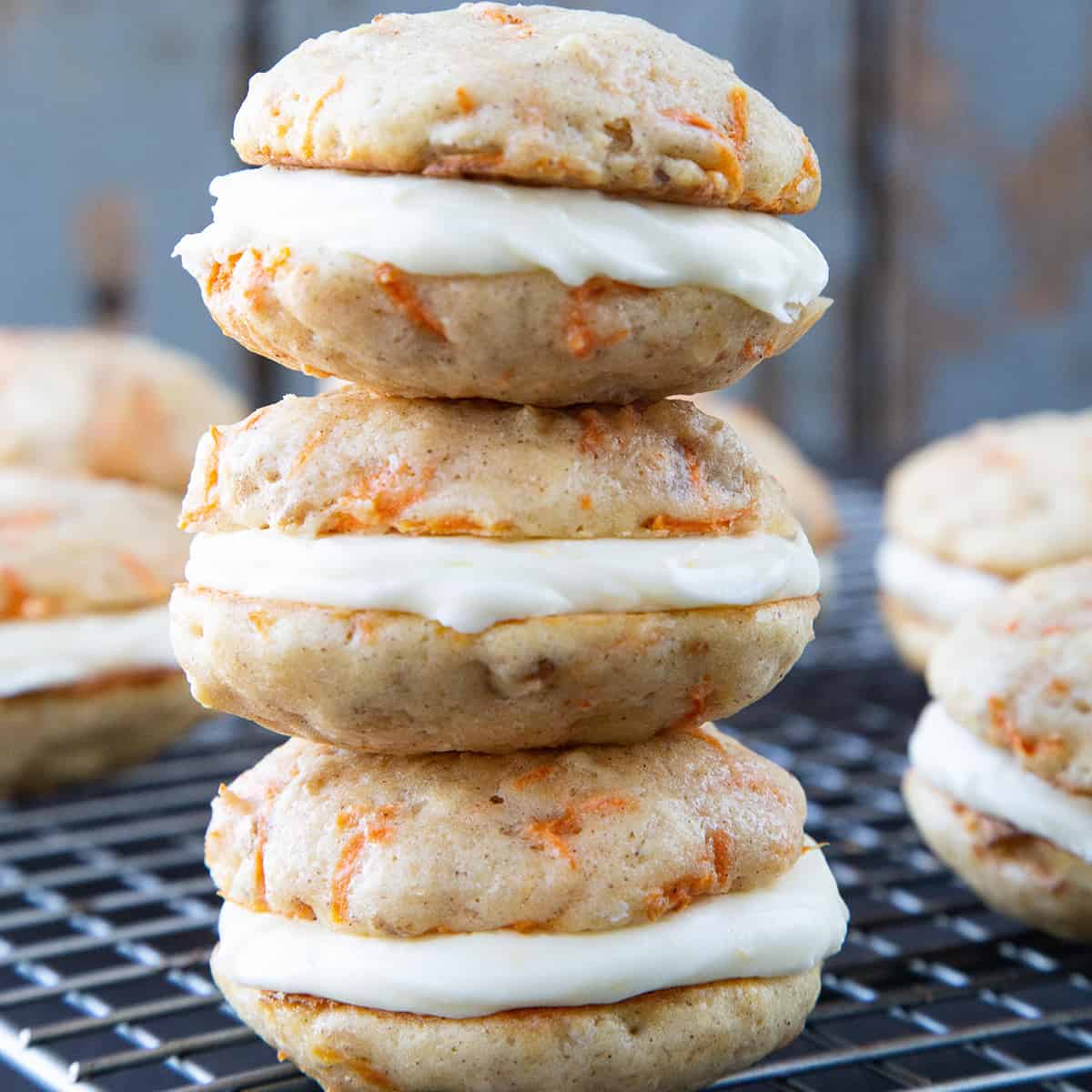 3 carrot cake whoopie pies stacked on a wire rack.