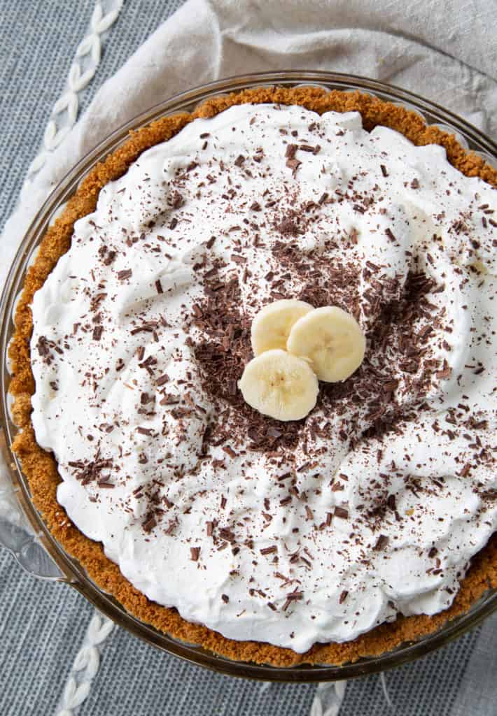 whole banoffee pie topped with whipped cream, banana slices, and chocolate shavings.