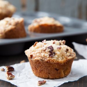 rhubarb muffin on a square of white parchment, with a muffin tin and more muffins in the background.