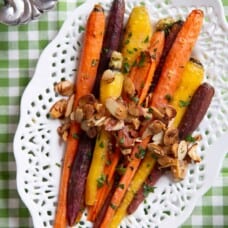 roasted glazed carrots with sliced almonds on a white serving platter with a cut-out pattern around the edges.